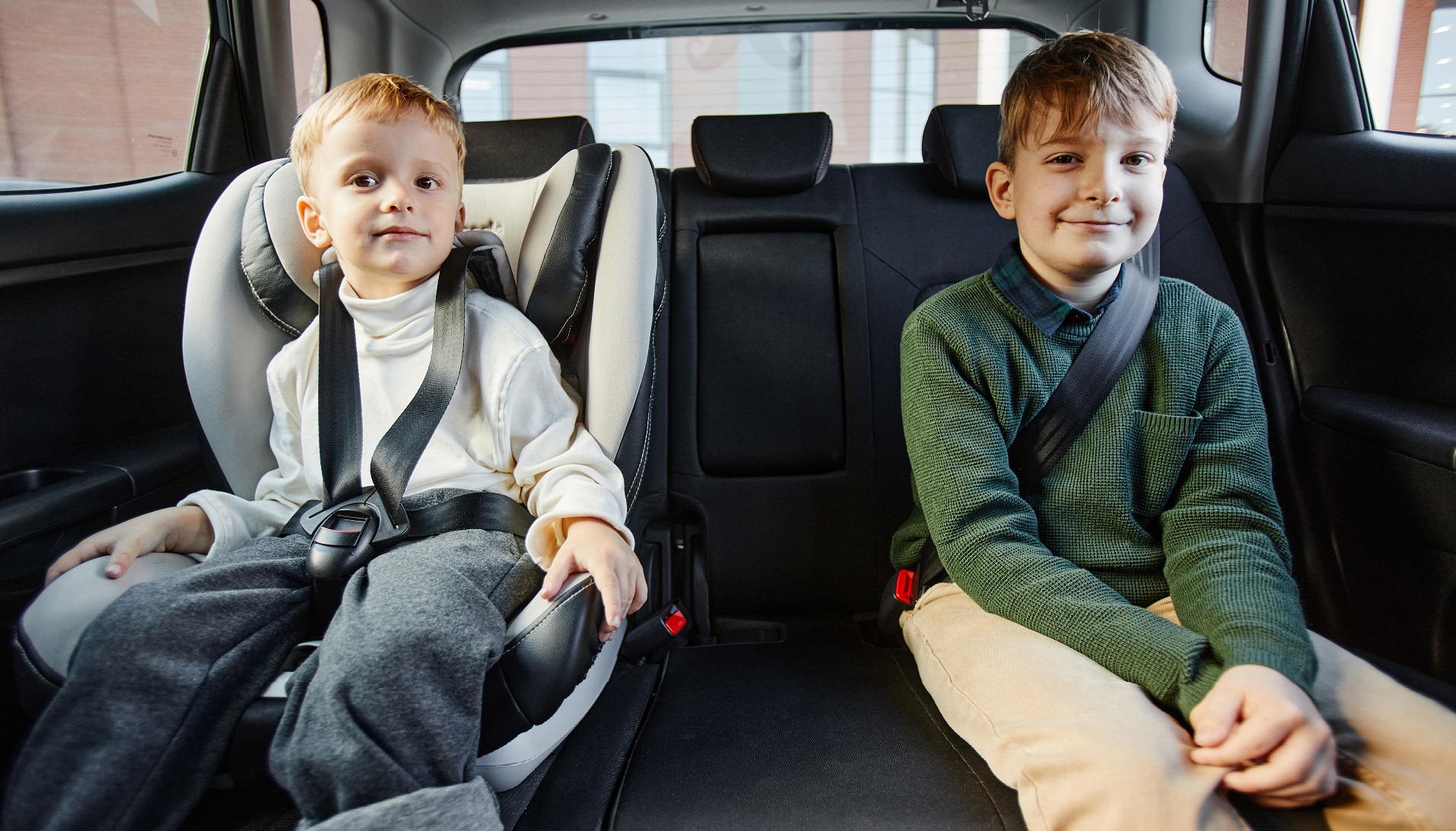 Portrait of two boys sitting in back seat of family car with safety belts and looking at camera